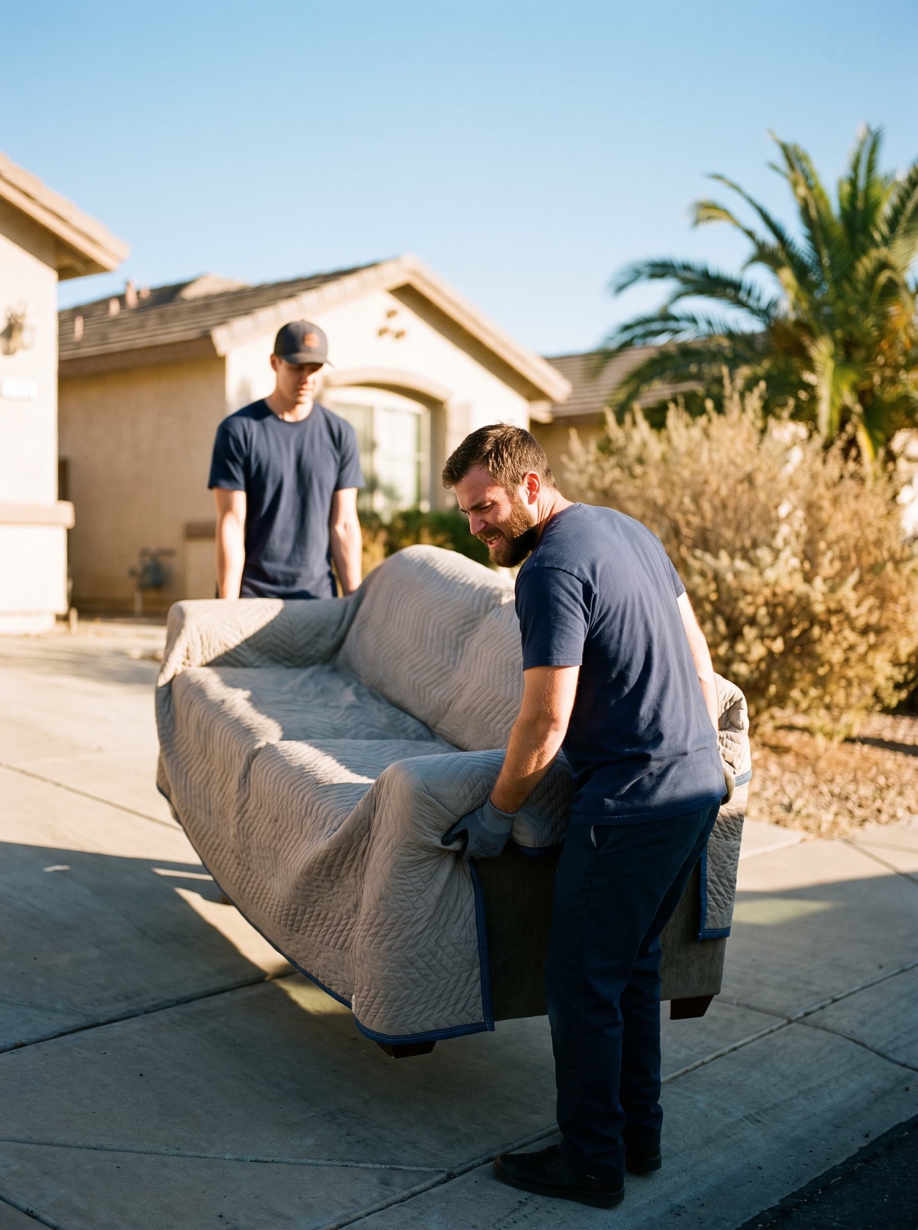 Two Upland Movers crew members carrying a sofa wrapped in a padded moving blanket